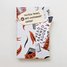 Gift-wrapped banned book in white and red ‘Read Banned Books’ paper with tag reading “Political themes, anti-government content.”