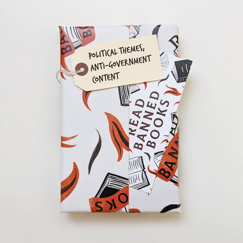 Gift-wrapped banned book in white and red ‘Read Banned Books’ paper with tag reading “Political themes, anti-government content.”
