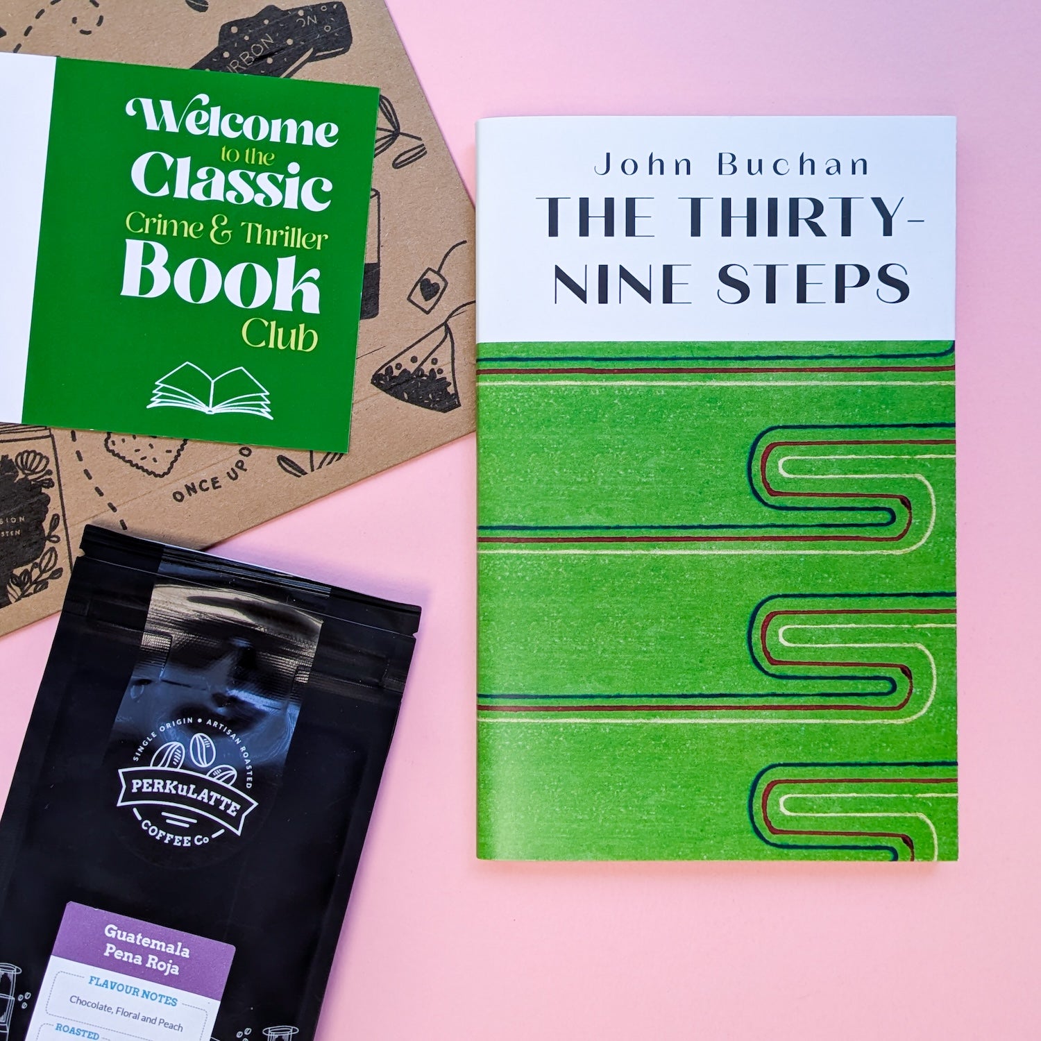 Classic crime and thriller book subscription flat lay including The Thirty-Nine Steps paperback, coffee sachet, and welcome card.