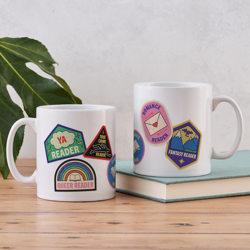 White ceramic mug featuring six colourful merit badge-style illustrations for different book genres: True Crime, Classics, YA, Fantasy, Queer, and Romance.
