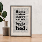 Framed book page print with the quote “Home is where there’s a stack of books by the bed” on a vintage book page background.