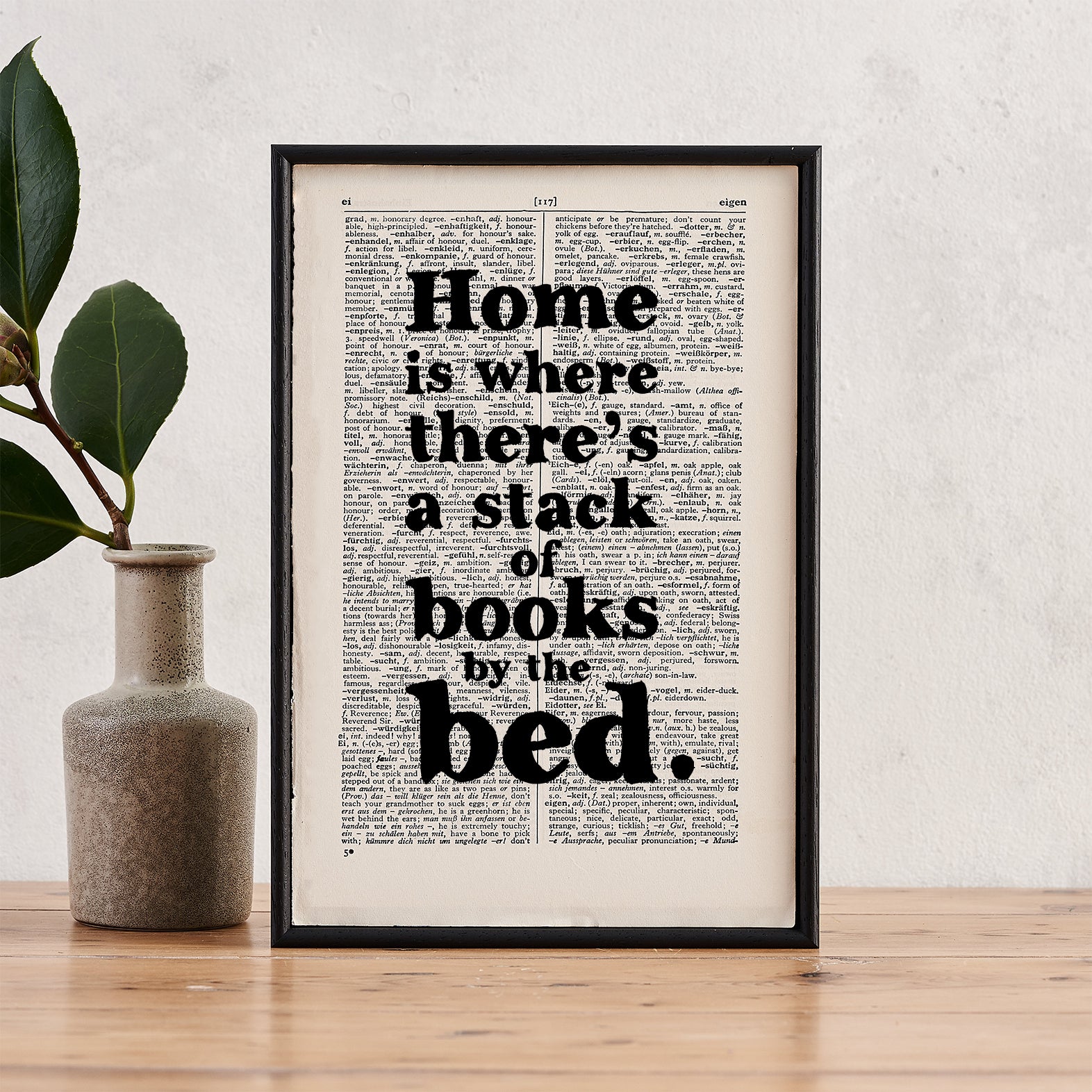 Framed book page print with the quote “Home is where there’s a stack of books by the bed” on a vintage book page background.