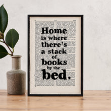 Framed book page print with the quote “Home is where there’s a stack of books by the bed” on a vintage book page background.