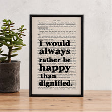 Framed book page print with the quote “I would always rather be happy than dignified” from Jane Eyre, styled with a potted plant on a wooden surface.

