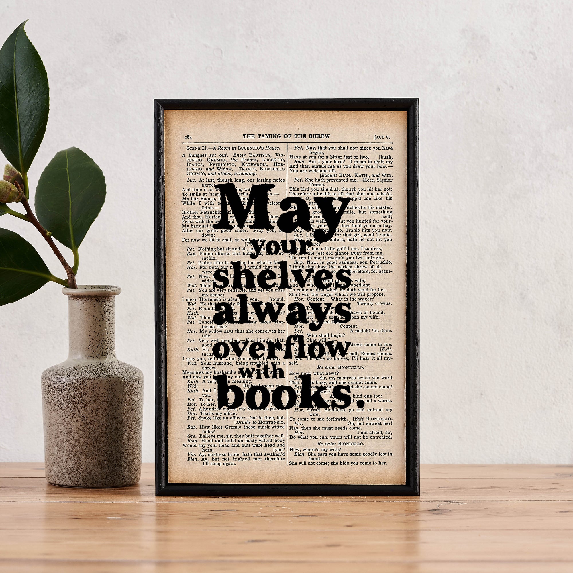 Framed book page print with the quote “May your shelves always overflow with books” printed in black text. 