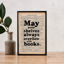 Framed book page print with the quote “May your shelves always overflow with books” printed in black text. 