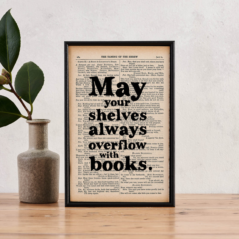 Framed book page print with the quote “May your shelves always overflow with books” printed in black text. 