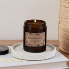 Pemberley candle in amber glass jar with floral kraft label, lit and resting on a speckled ceramic dish beside a Bookishly lid and matches