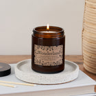 Wonderland candle in amber glass jar with whimsical floral label, lit and resting on a speckled ceramic tray beside matches and a Bookishly lid